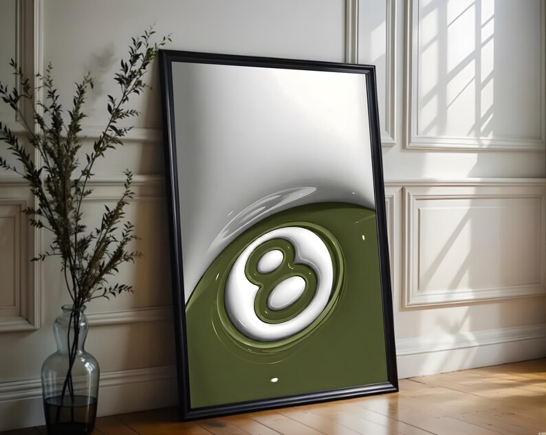 May include: Framed art print featuring a stylized 8-ball design. The artwork has a glossy finish with a white and olive green color scheme. The print is in a black frame and leans against a white wall.