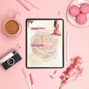May include: A digital tablet with lined paper and the text "Struggles/Surrendered: (My Letting go)" and "Placed in God's Hands (My Trusting Him to Take Over)". The tablet is surrounded by pink pens, a coffee cup, a camera, and pink macarons.