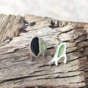 Puede incluir: Un par de pendientes de plata con esmalte negro y verde. Los pendientes tienen forma de figuras abstractas.