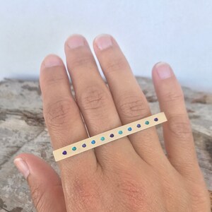 Puede incluir: Anillo de oro con una fila de piedras turquesa y moradas. El anillo está diseñado para ser usado en varios dedos.