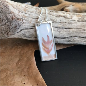 Puede incluir: Un collar de cadena de plata con un colgante rectangular que presenta un diseño floral abstracto rosa y naranja encapsulado en resina transparente.