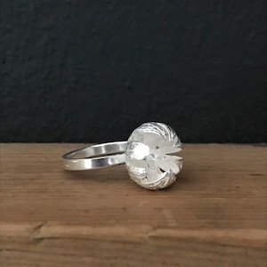 Puede incluir: Un anillo de plata con una parte superior redonda y abovedada texturizada.