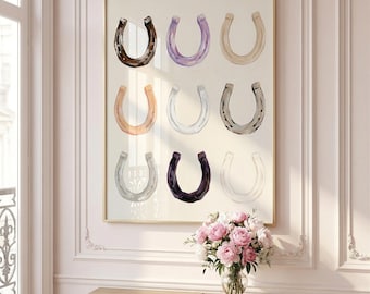 May include: A framed print featuring nine watercolor horseshoes in various colors, including brown, purple, and silver. The artwork is displayed on a light-colored wall above a gold console table with a vase of pink flowers.