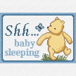 May include: A blue and white framed cross-stitch design featuring a cartoon bear with a butterfly and the text "Shh... baby sleeping".