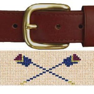 Puede incluir: Un cinturón tejido beige con una correa de cuero marrón y una hebilla dorada. El cinturón presenta un patrón repetido de remos cruzados con acentos rojos, azules y blancos.