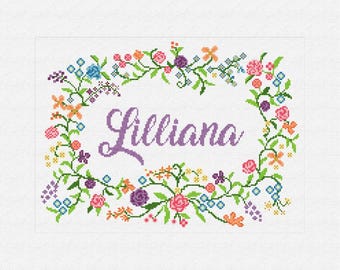 May include: A cross-stitch design featuring the name "Lilliana" in purple script, surrounded by a floral wreath. The wreath includes pink, orange, purple, and blue flowers with green leaves, set against a white background.