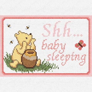 May include: A pink and white cross-stitch design featuring Winnie the Pooh holding a pot of honey. The text "Shh... baby sleeping" is stitched in pink.