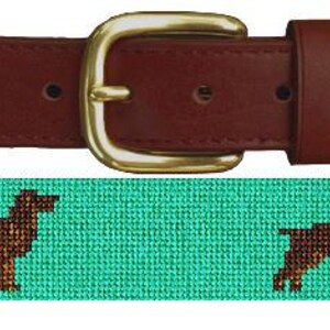 May include: A brown leather belt with a gold buckle. The belt is decorated with a repeating pattern of brown dogs on a teal background.