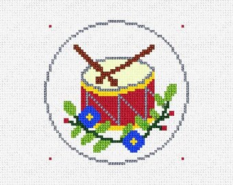 May include: A red and yellow toy drum with two drumsticks crossed over the top. The drum is surrounded by a green leafy garland with blue flowers.