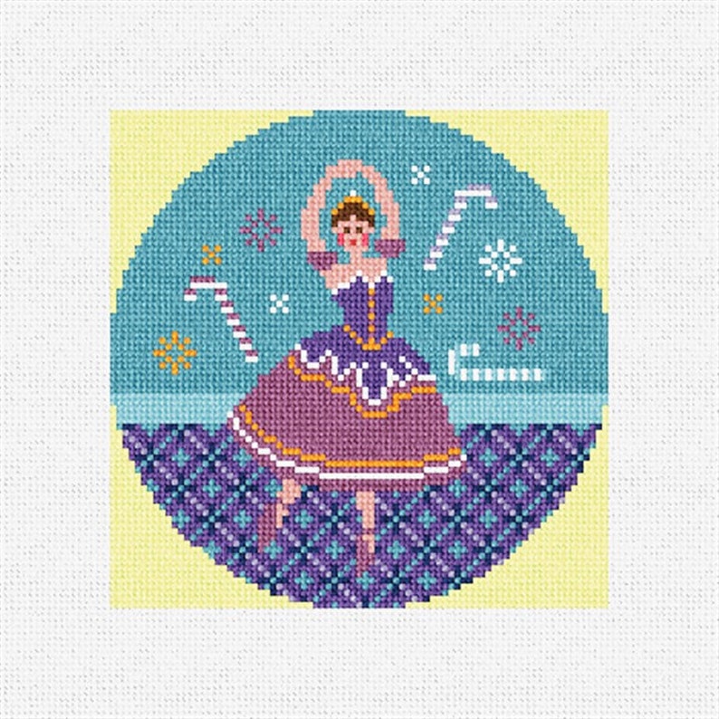 May include: A circular cross-stitch pattern featuring a ballerina in a purple and gold dress, dancing on a blue and purple patterned stage. The background is a light blue circle with white snowflakes and candy canes.