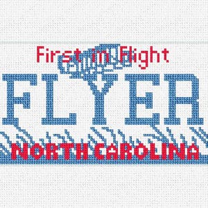 May include: Cross-stitch design of a license plate with the words "First in Flight" and "FLYER" in red and blue. The text "NORTH CAROLINA" is also in red. The design is on a white background.