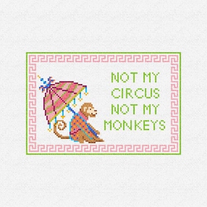 May include: A cross-stitch pattern on white fabric featuring a brown monkey holding a pink and green striped umbrella. The text reads NOT MY CIRCUS NOT MY MONKEYS in green letters. The design is enclosed in a pink Greek key border.
