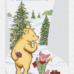 May include: A Christmas stocking featuring a cross-stitch design with the name "Alexander" in blue. The scene includes a yellow bear and a pink pig, with a decorated Christmas tree and snow-covered ground. A red gift box is also present.