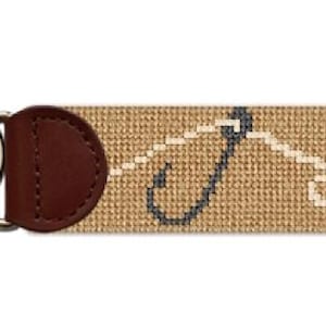 Peut inclure: Un porte-clés en point de croix beige avec un dos en cuir marron foncé et des anneaux de clés argentés. Le motif en point de croix présente un motif répétitif en blanc et bleu foncé. Un accessoire élégant pour les clés.