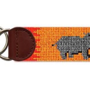 Może przedstawiać: Brelok do kluczy ze skórzanym paskiem w kolorze brązowym i podwójnym kółkiem. Pasek ma kolorowy, tkany wzór z szarym hipopotamem.