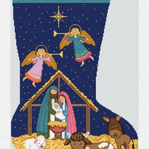 Pode incluir: Um desenho de ponto cruz de meia de Natal com uma cena de natividade. O desenho inclui a palavra "Gloria", anjos, uma estrela e a Sagrada Família em um estábulo, com uma vaca, um burro e um cordeiro.