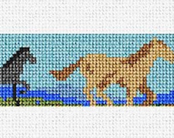 May include: A cross-stitch pattern featuring a scenic landscape with mountains, a blue lake, and four horses. The horses are brown, black, tan, and white. The background includes green trees and a blue sky.
