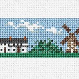 May include: A cross-stitch pattern featuring a coastal scene with a lighthouse, houses, a windmill, and a boat. The scene is set against a blue sky with white clouds.