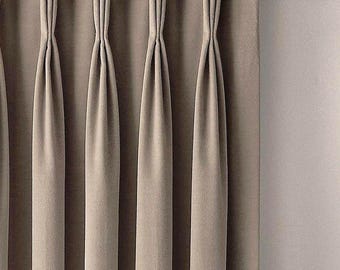 May include: A taupe-colored curtain panel featuring a pinch pleat header style. The fabric is suspended from a dark bronze metal curtain rod by circular rings. The curtain hangs in vertical folds, creating a structured and uniform appearance.