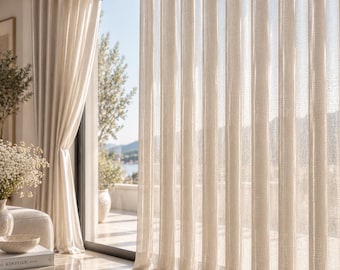 May include: Floor-to-ceiling off-white sheer curtains with a subtle vertical weave texture. These curtains feature a grommet top header and hang in uniform, pleated folds, allowing soft light to filter through the fabric into the room.