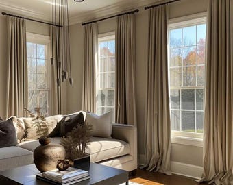 May include: A living room featuring floor-to-ceiling beige curtains on dark rods, a light-colored sofa with dark gray and beige throw pillows, and a dark square coffee table holding a round brown vase, books, and a small decorative object.