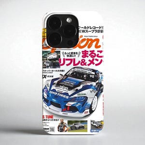 Op de afbeelding: Witte telefoonhoes met een tijdschriftomslagontwerp. De omslag toont een blauw-witte raceauto met Japanse tekst en de woorden "TOYO TIRES". De hoes heeft een camera-uitsparing en een glanzende afwerking.