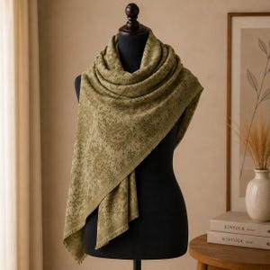 Peut inclure: Une écharpe vert olive ornée d'un motif floral et de médaillons ton sur ton détaillés. L'écharpe est drapée sur un buste de mannequin noir et présente un aspect doux et texturé avec des bords effilochés le long de l'ourlet inférieur.