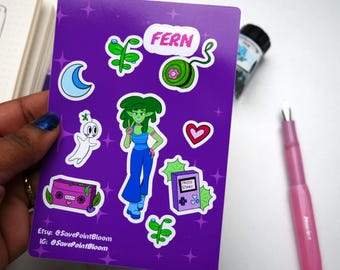 May include: A purple sticker sheet with cartoon illustrations of a green-haired character, a ghost, a moon, and a retro game console. The word "FERN" is at the top. A pink pen and ink bottle are also visible.