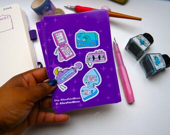 May include: A stack of purple stickers with retro-themed illustrations, such as a flip phone, camera, and perfume bottle. The stickers have a white border and star decorations. The Etsy shop name is visible on the stickers.
