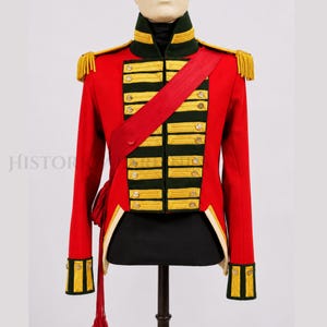 Puede incluir: Una chaqueta militar roja con adornos dorados, charreteras y botones. La chaqueta presenta un cuello alto, detalles verdes y dorados y una faja roja. La chaqueta se exhibe en un maniquí, mostrando su diseño histórico.