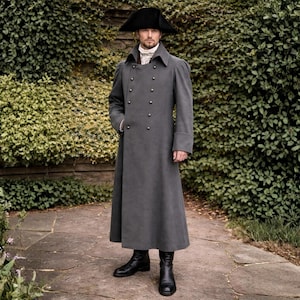 Könnte beinhalten: Ein langer, grauer Mantel mit doppelreihigem Design und großen Knöpfen. Der Mantel hat einen hohen Kragen und wird mit einem schwarzen Hut und Stiefeln kombiniert. Das Outfit erinnert an historische Militärkleidung.