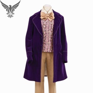 Puede incluir: Un abrigo de terciopelo morado con solapas, usado sobre una camisa con estampado floral, pantalones color canela y una pajarita color canela. El abrigo tiene un diseño largo y entallado con cierre de botón. El conjunto se muestra sobre un fondo blanco.