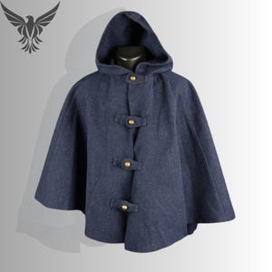 May include: A navy blue hooded cape with three decorative gold-colored clasps. The cape is made of a textured fabric and has a hood. The garment is displayed on a mannequin.