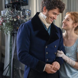 May include: A man in a navy blue coat with black velvet lapels and gold buttons, paired with a white cravat. A woman in a light blue dress and white gloves smiles at him. The scene suggests a period drama.