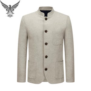 May include: A light grey blazer with a mandarin collar and four dark brown buttons. The blazer has two front pockets and a chest pocket. The sleeves are long and the fabric appears to be a wool blend. A bird logo is in the upper left corner.