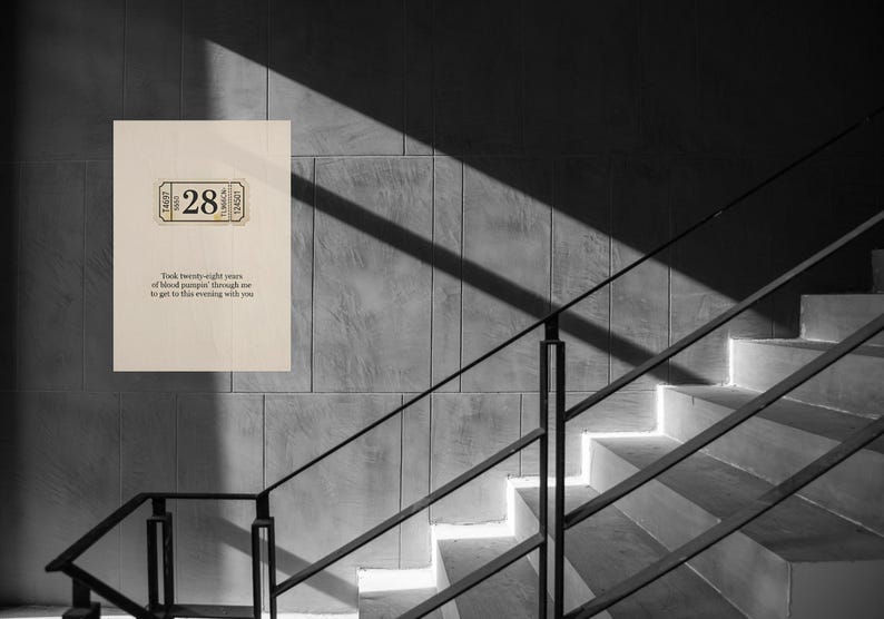 May include: A black and white photograph of a wall with a wooden sign and a staircase. The sign has a ticket design with the number 28 and text below. The text reads, "Took twenty-eight years of blood pumping through me to get to this evening with you."