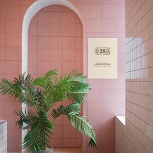 May include: A room with pink square tiles and a white arched doorway. A green potted plant is in the foreground. A framed print with the number 28 and text is on the wall.