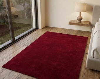 May include: A rectangular area rug in a deep, solid shade of burgundy red. The rug features a short, dense pile texture and is positioned flat on a light-toned wooden floor, covering a significant portion of the floor space in the room.
