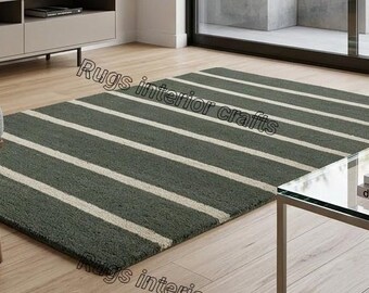 Op de afbeelding: Een rechthoekig, groen tapijt met brede, horizontale witte strepen. Het tapijt ligt op een houten vloer, met een moderne stoel en salontafel op de achtergrond. Het tapijt is een item voor interieurdecoratie.