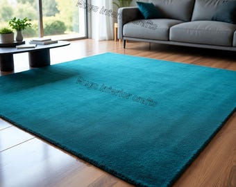 May include: A large, rectangular teal rug dominates the foreground, with a soft, plush texture. The rug is placed on a hardwood floor, and a gray sofa with teal cushions is visible in the background. The room has large windows.