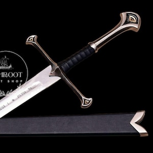 Puede incluir: Una espada plateada y negra con un mango envuelto en cuero y una guarda decorativa. La hoja tiene texto grabado. La espada está parcialmente enfundada en una vaina negra. El fondo es negro.