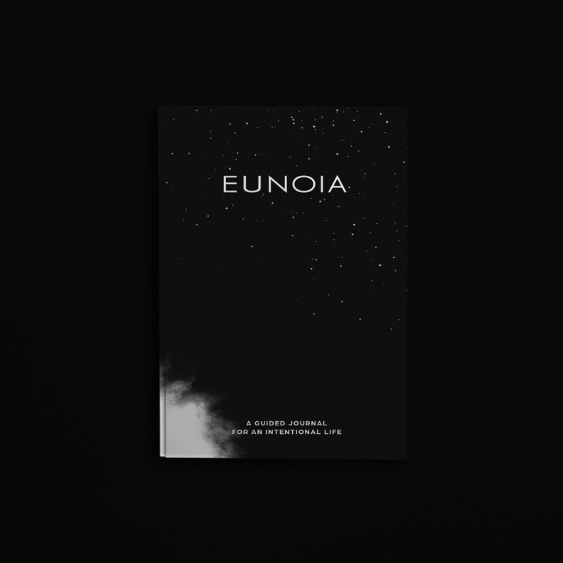Pu&ograve; includere: Un diario in bianco e nero con la parola "EUNOIA" in lettere bianche in alto. La copertina presenta un design a notte stellata. Il testo "A GUIDED JOURNAL FOR AN INTENTIONAL LIFE" &egrave; in basso.