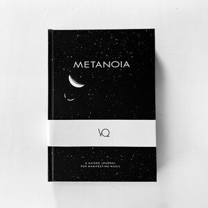 May include: A black journal with the word "METANOIA" in white, a crescent moon and stars design. The journal is wrapped with a white band and includes the text "A GUIDED JOURNAL FOR MANIFESTING MAGIC".
