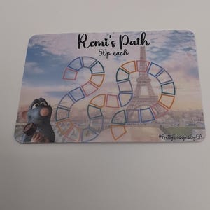 May include: A rectangular card with a board game design, featuring the text "Remi's Path". The game board includes a large number 20, the Eiffel Tower, and a cartoon rat. The card has a cloudy sky background.