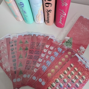 May include: A selection of colourful binders and Christmas-themed stickers. The binders are in teal, pink, and marble designs, with text such as "Birthdays" and "2026 Savings." The stickers feature Christmas trees, Santa, and other festive designs.