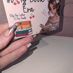 May include: A pink card with the text "In My Book Era" and a stack of books illustration. The card also features an illustration of a woman reading a book and the text "50p Per Letter £1 Per Book".