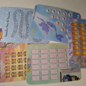 May include: A selection of money-saving challenge cards with various designs. Themes include "Toy Story", "The Lion King", and "Monster", plus a mermaid and pearl design. Each card has a unique layout for saving money, with amounts in British pounds.
