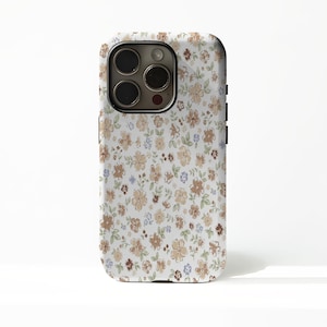 May include: A smartphone case featuring a repeating pattern of small, hand-drawn style flowers in shades of tan, brown, and light blue on a white background. The case has a rectangular cutout for a triple-lens camera system on the upper left.