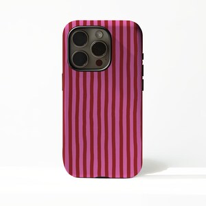 Puede incluir: Funda de teléfono con un patrón de rayas verticales en tonos alternos de rojo y rosa. La funda tiene un módulo de cámara con múltiples lentes y un marco negro.