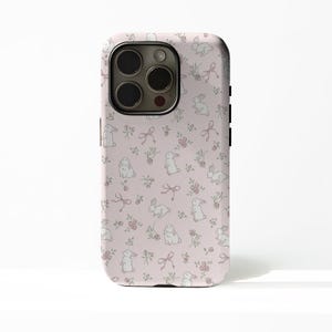 May include: A light pink phone case with a repeating pattern of white bunnies, pink bows, and small pink flowers. The case has a glossy finish and a camera cutout on the back.